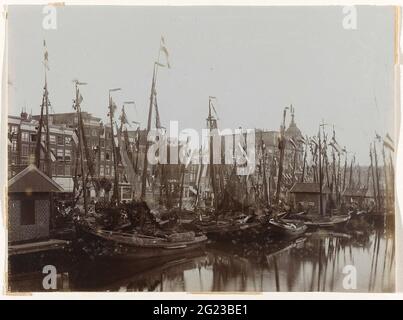 Boote im Damrak, geschmückt mit Fahnen, anlässlich der Einweihung der Königin Wilhelmina, Amsterdam, Niederlande. Die Boote im Damrak sind anlässlich der Einweihung der Königin Wilhelmina mit Fahnen geschmückt. Auch an den Häusern am Damrak und am Victoria Hotel (rechts) sind Flaggen ausgestreckt. Ganz auf der rechten Seite des Hauptbahnhofs, Amsterdam, Niederlande Stockfoto