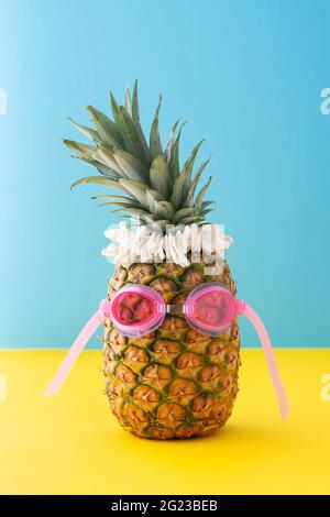 Ananas in rosa Schwimmbrille mit Muschelschalen aus der Nähe auf gelb-blauem Hintergrund, Sommerkonzept Stockfoto