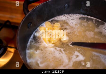 Kochen getrocknete Nudeln Formen in kochendem Wasser und Abtropfen Stockfoto