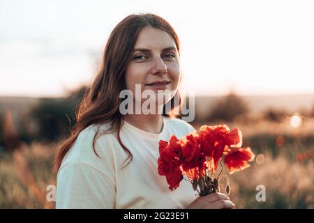 Frau Hand hält roten Mohnstrauß bei Sonnenuntergang auf dem Feld Stockfoto