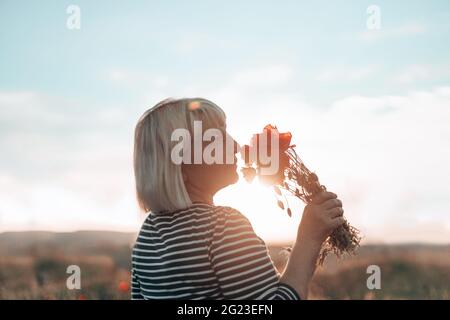 Kaukasische Frau Hand hält ein Bouquet von Mohnblume auf Wiese Hintergrund bei Sonnenuntergang. Tourismus, Reisen und gesundes Lifestyle-Konzept. Stockfoto