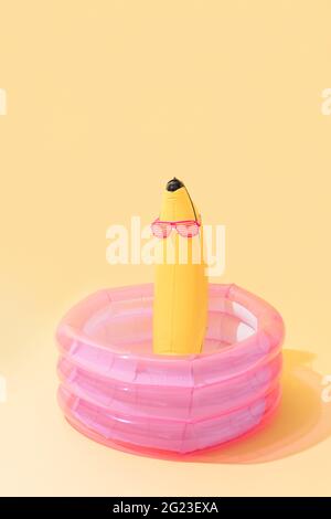 Kinderbecken mit einer bananenförmigen aufblasbaren Banane mit Sonnenbrille auf gelbem Hintergrund. Vertikales Bild Stockfoto