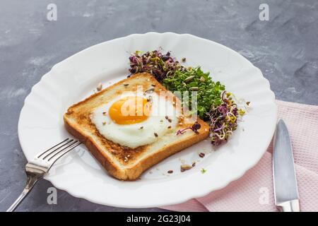 Ein Sandwich mit Ei im Loch des Brotes, Microgreens, gesunde Ernährung Frühstück, grauer Hintergrund Stockfoto
