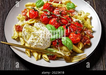 Italienische Caprese Pasta backen aus Pasta Penne, Speck, Kirschtomaten und Mozzarella-Käse, gekrönt mit zerfetzten Parmesan, frisches Basilikum auf einem Teller serviert Stockfoto