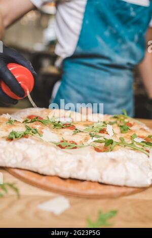 Küchenchef macht Pizza im Restaurant. Frisch zubereitete Pizza mit Kirschtomaten und Rucola Stockfoto