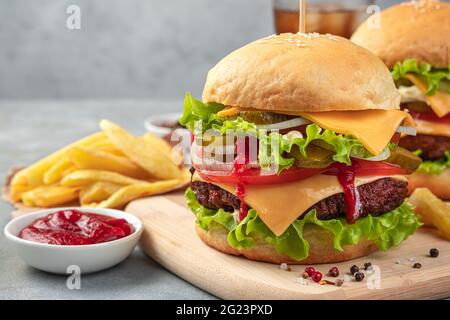 Großer Burger mit Rinderpastete, Käse, Sauce, Gemüse und Salat auf grauem Hintergrund. Seitenansicht, Nahaufnahme. Stockfoto