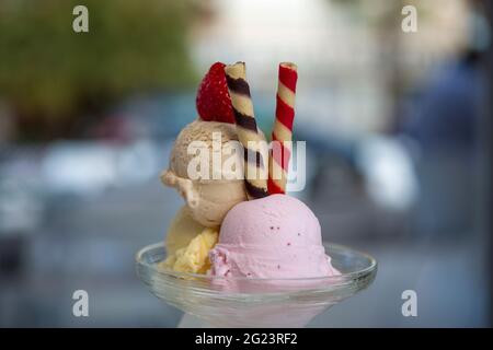 Drei Kugeln Eis in verschiedenen Geschmacksrichtungen und Farben in einem Glas mit unfokussierten Hintergrund, Stockfoto