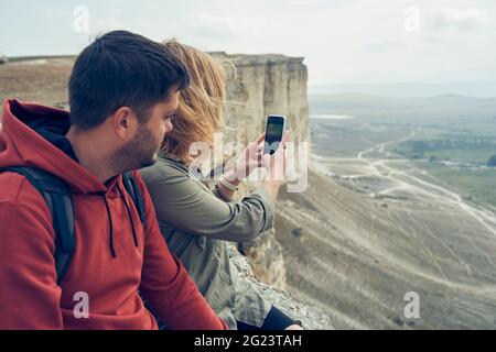 Das Paar sitzt auf den Steinen, ruht sich aus, fotografiert und genießt die Aussicht und die frische Luft. Wanderkonzept Stockfoto