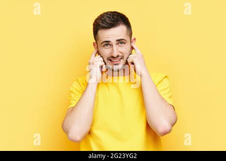 Schöner lustiger Mann, der seine Ohren mit Händen bedeckt, die Angst haben, schlechte Nachrichten auf gelbem Hintergrund isoliert zu hören Stockfoto