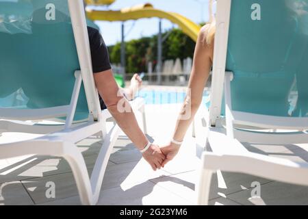 Mann und Frau liegen auf Sonnenliegen am Pool und halten die Hände in der Nähe Stockfoto