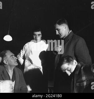 1960, historisch, abends und ein junger Krankenpfleger mit einigen älteren Patienten, die traditionelle Wollkleidung tragen, Fife, Schottland. Stockfoto