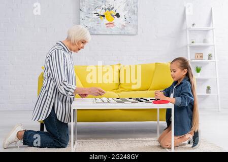 Kind spielt Dame mit älteren Großeltern auf dem Couchtisch Stockfoto