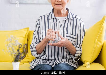 Beschnittene Ansicht einer älteren Frau, die zu Hause ein Glas Wasser hält Stockfoto