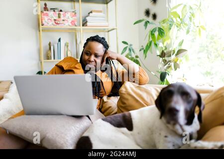 Frau, die mit Hund auf dem Sofa liegt und am Laptop arbeitet Stockfoto