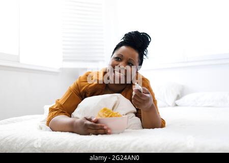 Frau, die im Bett Kartoffelchips isst Stockfoto