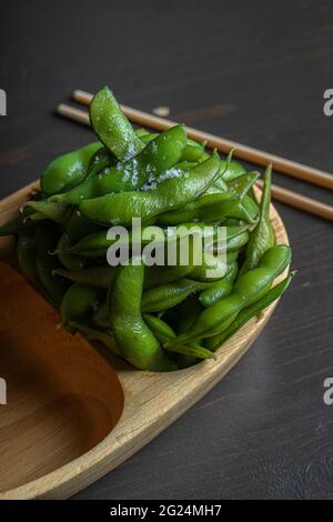 Bio-Lebensmittel in einer Holzschüssel gekocht. Traditionelle japanische Sojabohnen, edamame, gewürzt mit schwarzem Meersalz. Stockfoto