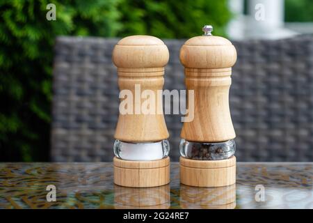 Salz- und Schwarzpfeffer-Shaker in einem Sommercafé, eine hölzerne Pfeffermühle auf einem Tisch in einem Restaurant. Gewürze, Zutaten beim Kochen Stockfoto