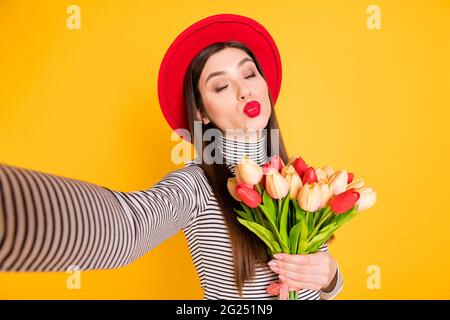 Foto von jungen attraktiven Mädchen pouted Lippen senden Luft Kuss halten Tulpen Bouquet machen Selfie isoliert über gelben Hintergrund Stockfoto