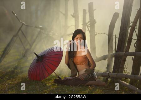 Frau, die auf dem Gras neben ihrem Sonnenschirm sitzt, Thailand Stockfoto