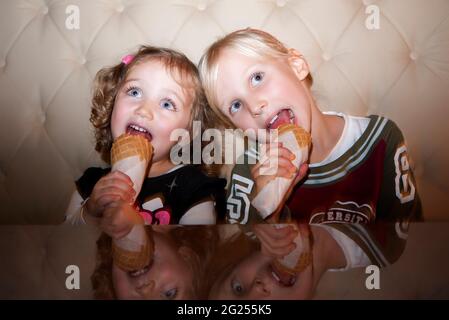 Zwei Mädchen sitzen auf einem Sofa und essen Eiszapfen Stockfoto