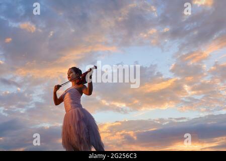 Frau, die bei Sonnenuntergang draußen steht und Geige spielt, Thailand Stockfoto