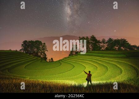 Mann, der in der Nacht unter der Milchstraße in terrassierten Reisfeldern steht, Mu Cang Chai, Yen Bai, Vietnam Stockfoto