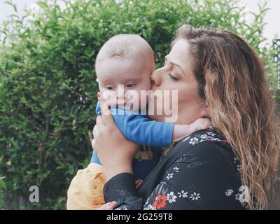 Mutter steht im Garten und küsst ihren kleinen Sohn Stockfoto