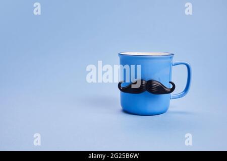 Kaffeetasse mit Schnurrbart und Fliege auf blauem Hintergrund. Happy Father's Day Konzept Stockfoto