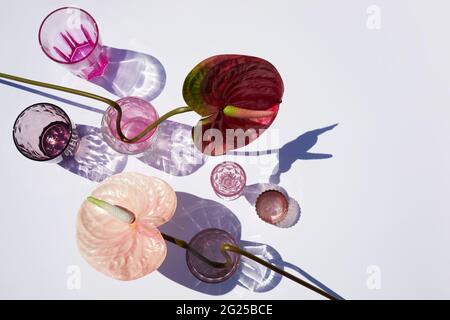 Sommerstill-Szene. Glitzernde rosafarbene Gläser Wasser oder Cocktails auf weißem Tischhintergrund bei Sonnenlicht. Lange harte Schatten. Urlaubskonzept Stockfoto
