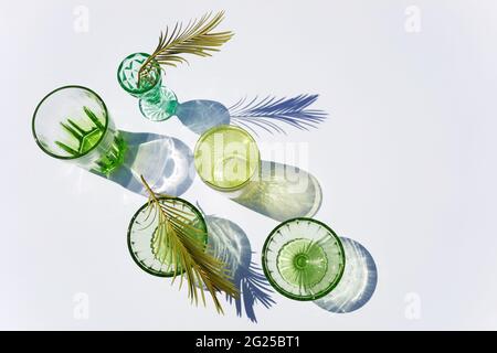 Sommerstill-Szene. Glitzernde grüne Gläser Wasser oder Cocktails auf weißem Tischhintergrund im Sonnenlicht. Lange harte Schatten. Urlaubskonzept Stockfoto