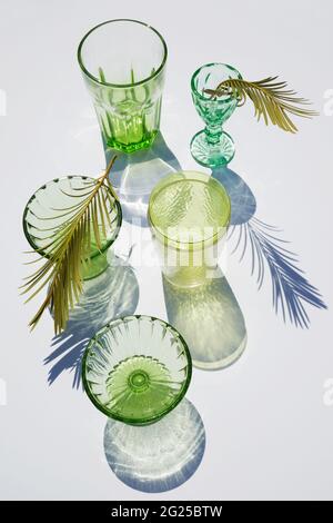 Sommerstill-Szene. Glitzernde grüne Gläser Wasser oder Cocktails auf weißem Tischhintergrund im Sonnenlicht. Lange harte Schatten. Urlaubskonzept Stockfoto