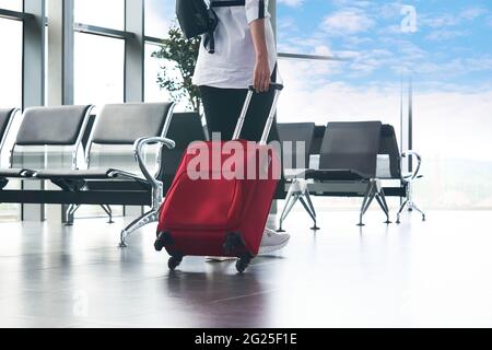 Eine Frau geht durch die Flughafenlounge direkt in den Himmel; Beine und Koffer aus der Nähe Stockfoto