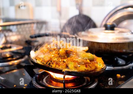 indische gemischte vegetable Gericht Sizzler mit Reis, Pommes frites, Kartoffeln, Gemüse Koteletts und Kohl auf Eisenschale gelegt, die auf einem Gasherd Flamme erhitzt Stockfoto