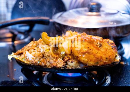 indische gemischte vegetable Gericht Sizzler mit Reis, Pommes frites, Kartoffeln, Gemüse Koteletts und Kohl auf Eisenschale gelegt, die auf einem Gasherd Flamme erhitzt Stockfoto