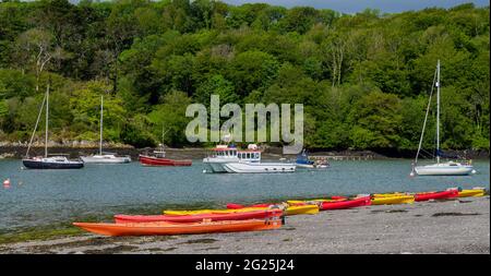 Kajaks, die am Kiesstrand mit Yachten in der Gezeitenmündung vor Anker liegen, wurden hochgefahren Stockfoto