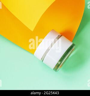 Glas mit kosmetischer Creme auf gelb-grünem Hintergrund, Draufsicht. Hautpflege, Feuchtigkeitscreme, kosmetisches Produkt, minimalistischer Stil Stockfoto