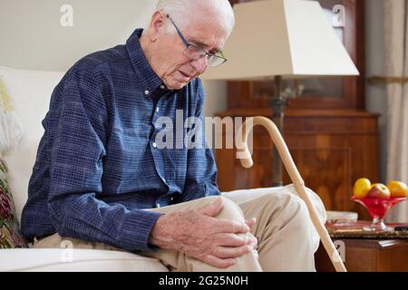 Älterer Mann, Der Zu Hause Auf Dem Sofa Sitzt Und An Knieschmerzen Durch Arthritis Leidet Stockfoto