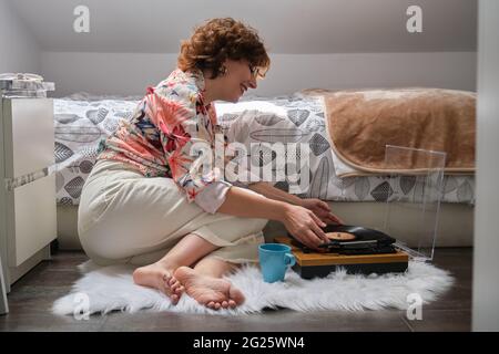 Junge Frau, die in ihrem Schlafzimmer eine Schallplatte auf den Plattenspieler legt Stockfoto