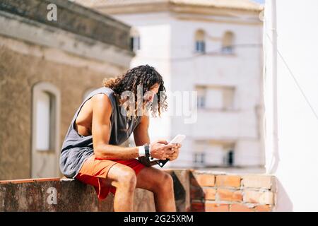 Langhaariger Athlet Mann mit Handy auf der Terrasse Stockfoto