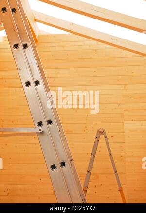 Leitern in einem teilweise gebauten Blockhaus aus Holz (Tanne), einem vorgeschnittenen Holzhaus, das vor Ort montiert wird. Konzentrieren Sie sich auf die Leiter im Vordergrund. Italien Stockfoto