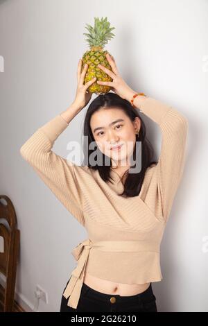 Junge asiatische Frau, die eine Ananas auf dem Kopf hält Stockfoto