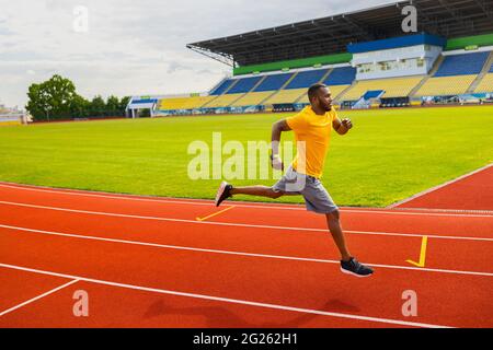 Professionell fokussiertes afro-amerikanisches Athletentraining auf der Rennstrecke im Stadion. Seitenansicht des schwarzen männlichen Sprinters, der auf dem läuft Stockfoto