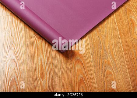 Auf dem Holzboden wird eine ausgeklappte fliederfarbene Yogamatte ausgeklappt. Draufsicht Stockfoto