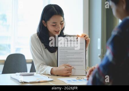 Vor dem Verkauf eines Hauses erklärt der Makler dem Kunden den Vertrag und weist auf die Unterschrift in der Dokumentation hin. Immobilienkonzept. Stockfoto