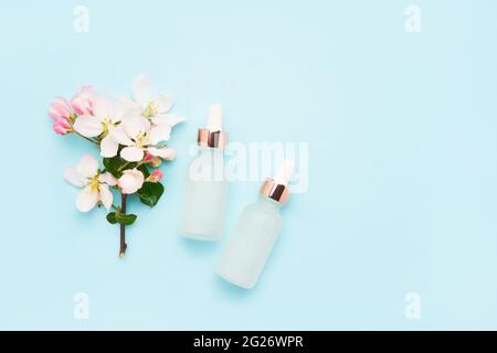 Zwei Tropfflaschen aus Glas für medizinische und kosmetische Zwecke und Apfelblütenblumen auf hellblauem Hintergrund. SPA-Konzept. Draufsicht, Kopierbereich Stockfoto