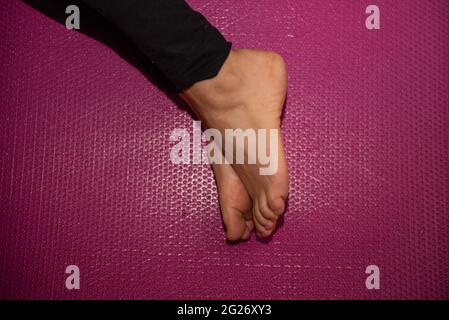 Hintergrund rosa Matte Pilates Frau Training Fuß Gesundheit Übung in fit schwarz Sportbekleidung zu Hause Stockfoto