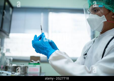 Der junge Arzt in einer weißen Uniform, der ein Gesicht und einen Gesichtsschutz trägt, bereitet eine Spritze zur Impfung von Menschen im medizinischen Zentrum vor. Stockfoto
