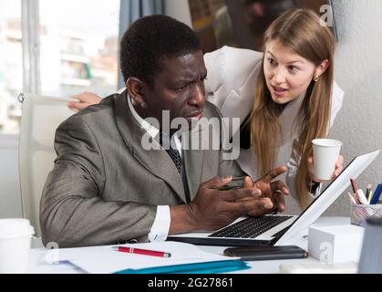 Junge Managerin, die den Mann während der Arbeit am Laptop unterstützt Stockfoto