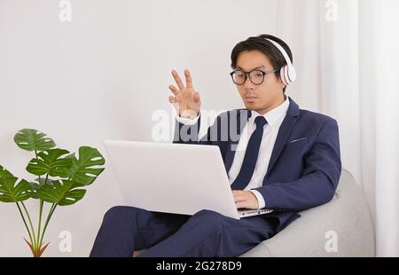 Asiatischer Finanzberater trägt Kopfhörer und Brille Videokonferenz mit Kunden im Heimbüro. Geschäftsmann arbeiten zu Hause für soziale Distanz oder zu Hause Stockfoto