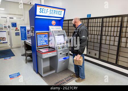 Ein Mann mit einer Maske verwendet den Self-Service-Kiosk, um ein Paket an der Northwood Station des US-Postamtes in Fort Wayne, Indiana, USA, zu versenden. Stockfoto